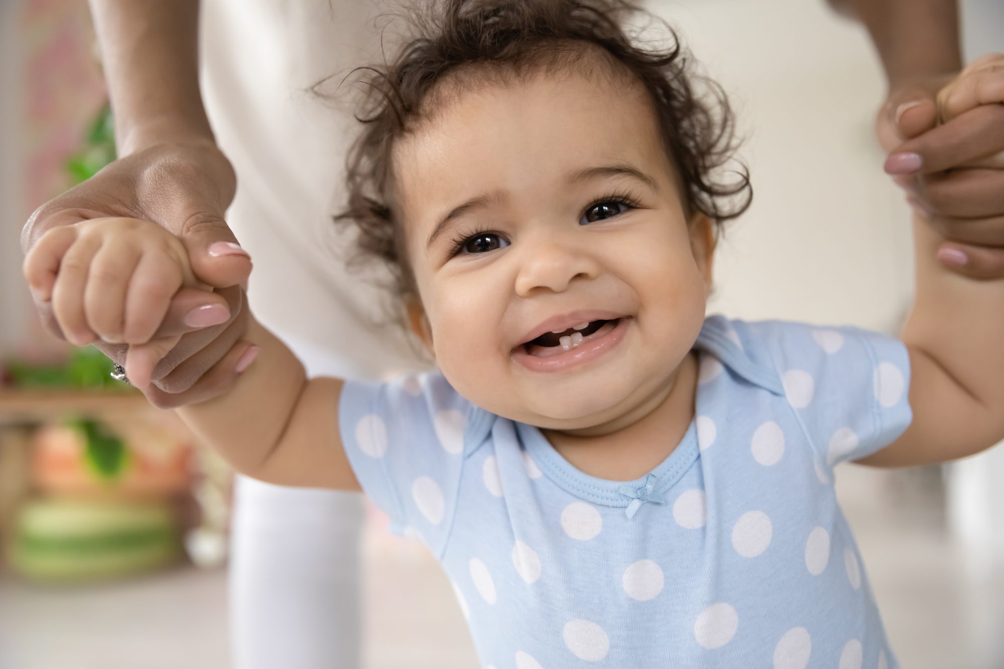 A toddler taking first steps, holding a teacher&rsquo;s hands